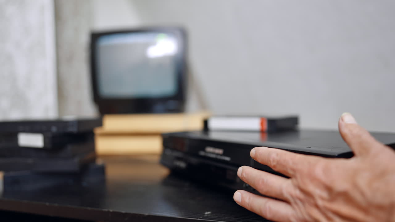 Caucasian hand presses the buttons on the panel of DVD player. Lines run on the screen at backdrop in blur. Tape shoots out of the device. Close up