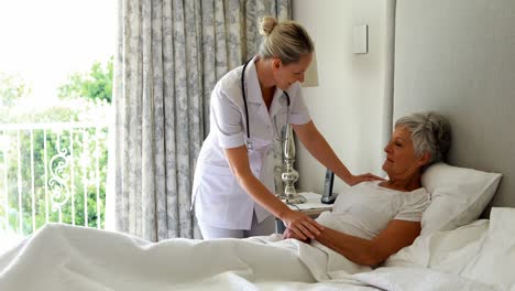 Female-doctor-comforting-senior-woman-on-bed-in-bedroom