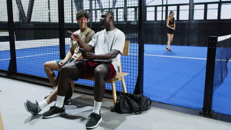 diverse friends relaxing on bench, watching padel match, enjoying leisure time on indoor court