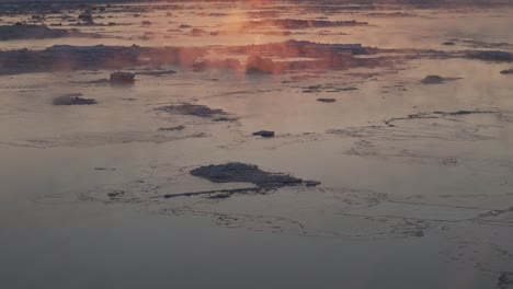 cinematic tracking shot of golden fog floating over large frozen lake, dusk