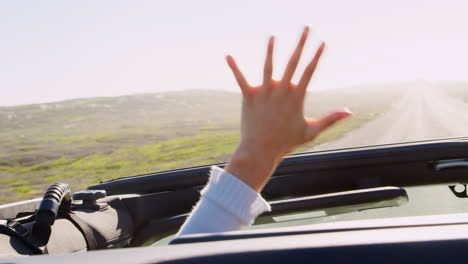 Adult-friends-reaching-hands-out-of-sunroof-of-driving-car