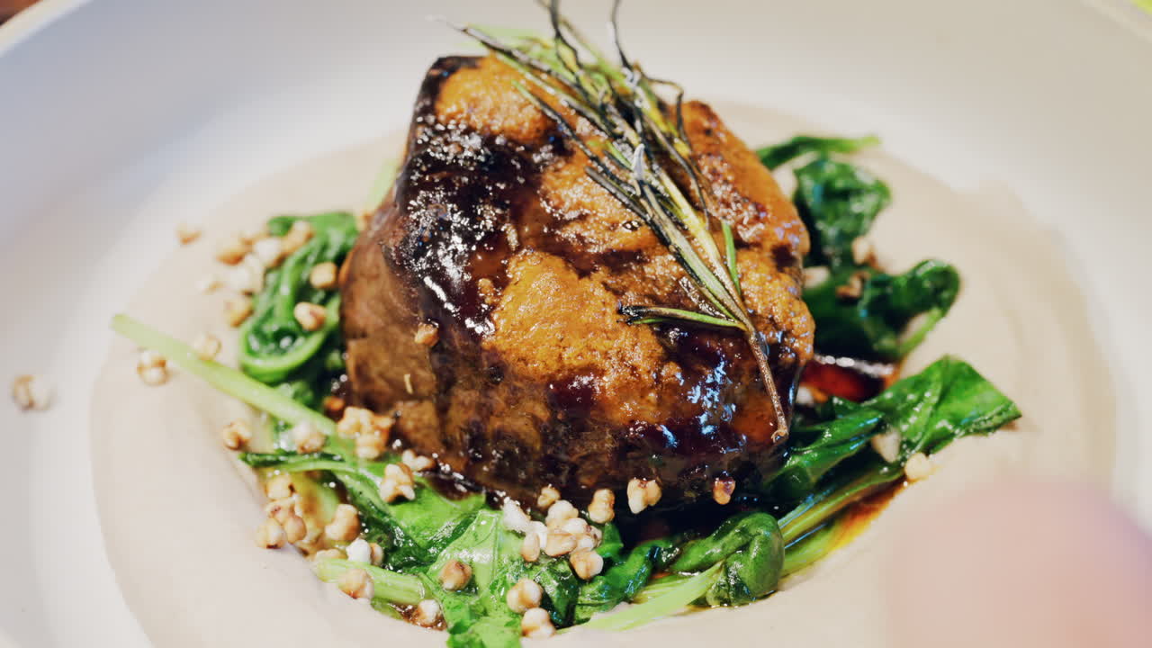 Close up of a beautifully plated beef filet, topped with a golden crust and garnished with rosemary