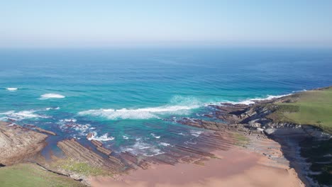 steady-aerial-shot-of-a-beautiful-sunny-hazy-sea-coast-of-Playa-de-Tagle,-surf-beach-in-Spain,-near-Bilbao