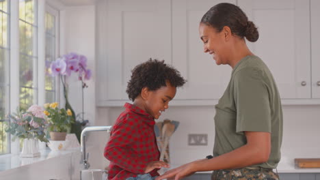 army mother in uniform home on leave giving son high five in family kitchen