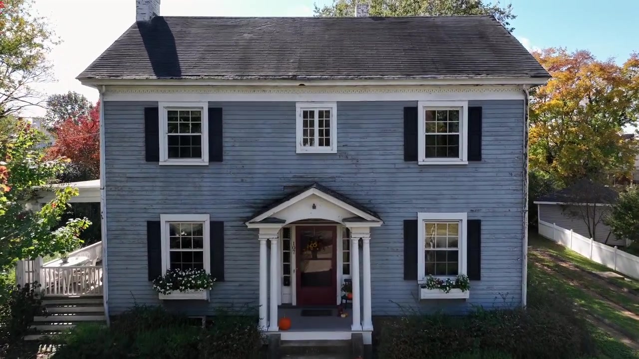 Aerial flyover historic single family house in American town. Halloween season with pumpkins on entrance door. Approaching shot. October day in fall season.