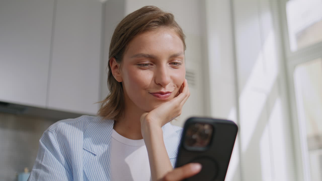 Home girl browsing smartphone in sunny kitchen. Portrait woman using cellphone
