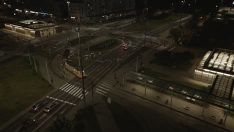 Aerial-view-of-a-modern-electric-streetcar-passing-through-the-traffic-circle-at-night,-Poland,-Warsaw