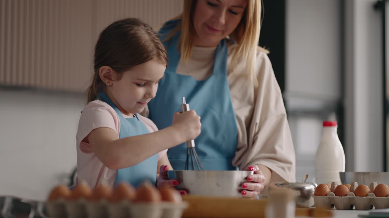 little girl is learning to cook and helping her mother in kitchen cooking in home woman and her daughter