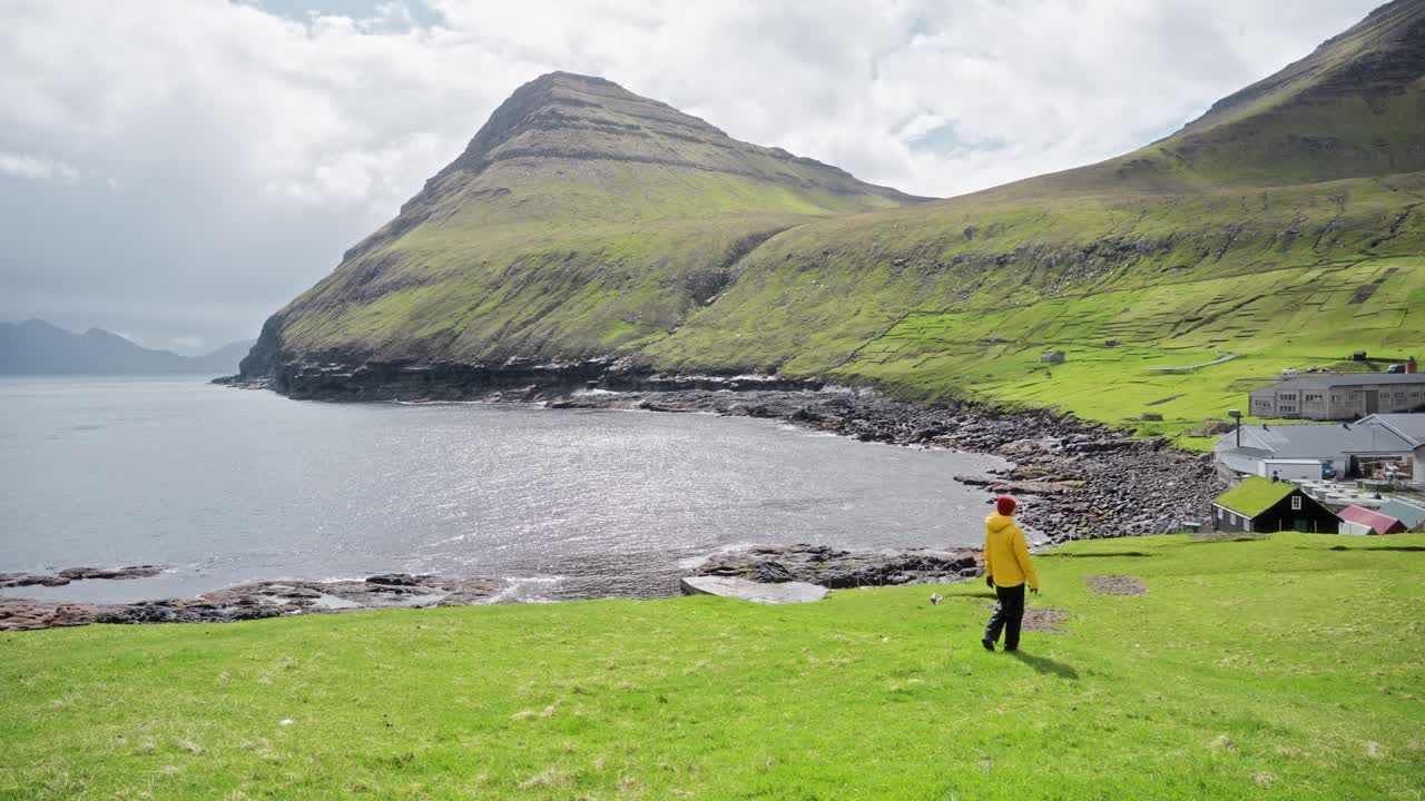 A person walks on green hills near Gjógv, Faroe Islands, under a sunny sky