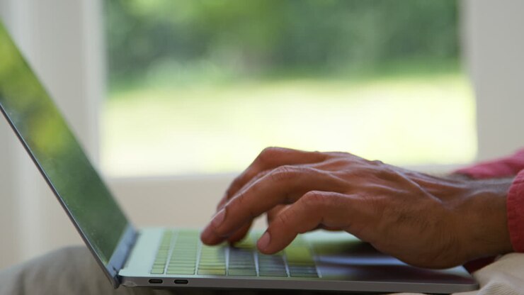 Close Up Of Fingers On Laptop Keyboard As Man Works From Home Sitting On Floor In Lounge