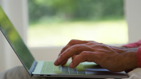 cerrar los dedos en el teclado de la computadora portátil como el hombre trabaja desde casa sentado en el suelo en la sala