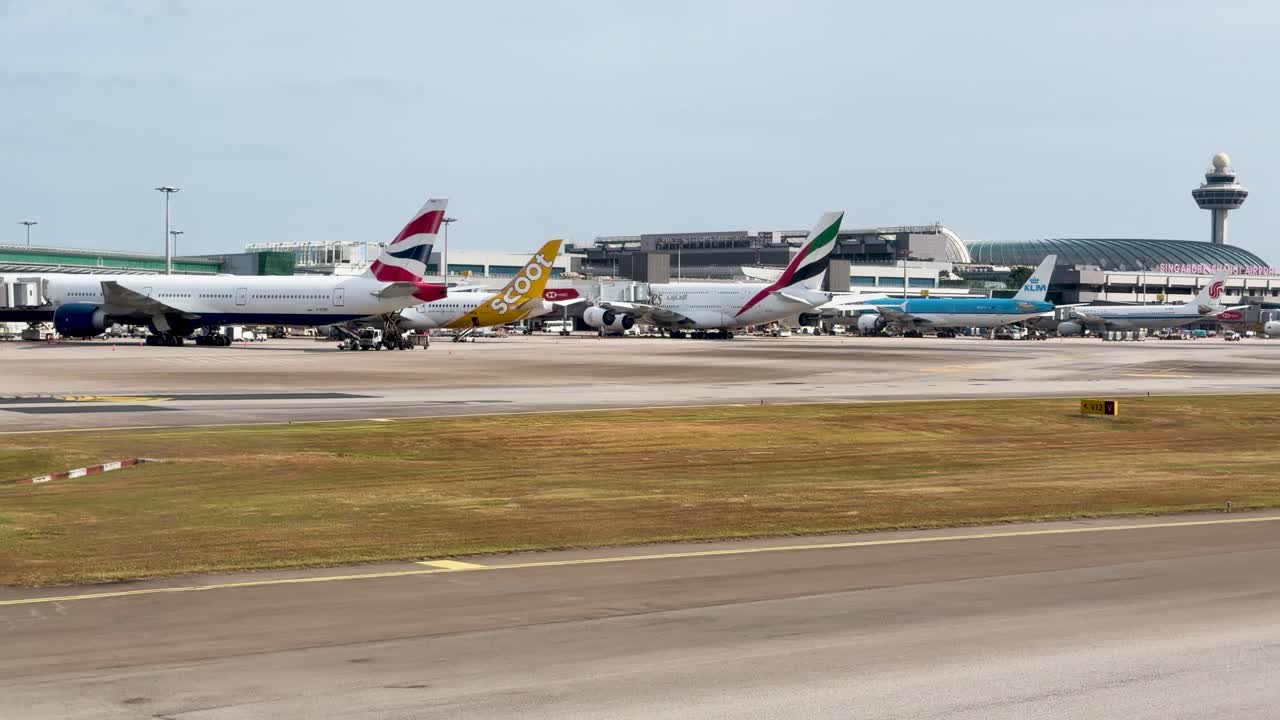Inquadratura ampia di numerosi aerei commerciali parcheggiati ai gate del terminal in pieno giorno.