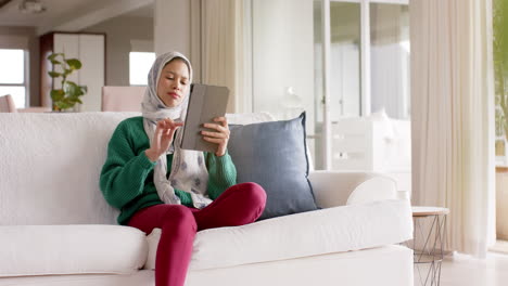 Biracial-Frau-Im-Hijab-Mit-Tablet-Auf-Dem-Sofa-Zu-Hause-Mit-Kopierplatz,-Zeitlupe