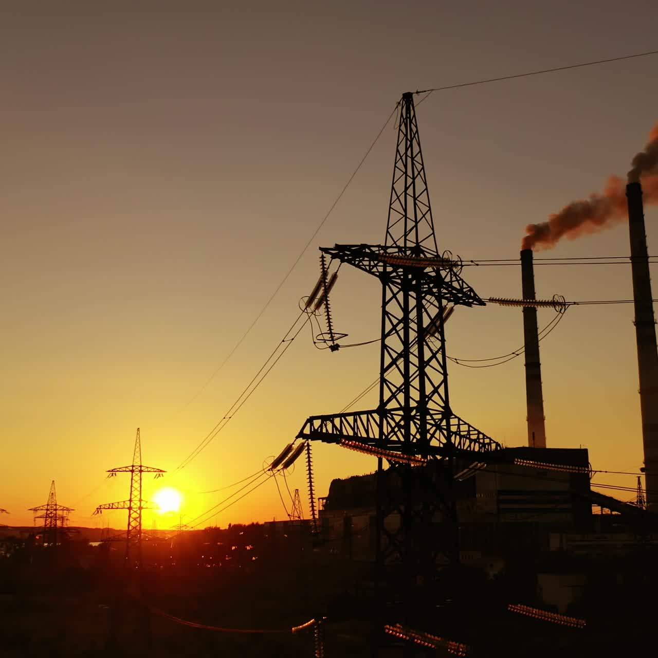Industrial factory and electricity pylons at sunset. Silhouettes of high voltage power lines against the setting sun. Industrial minimalist landscape.