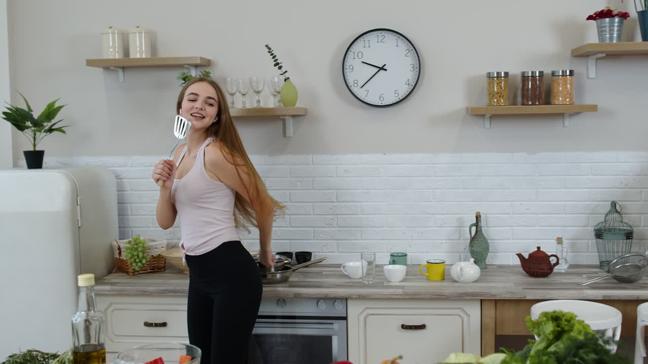 Ragazza vegana felice con la vita sottile che balla e canta in cucina. Concetto di alimentazione a base di verdure crude.