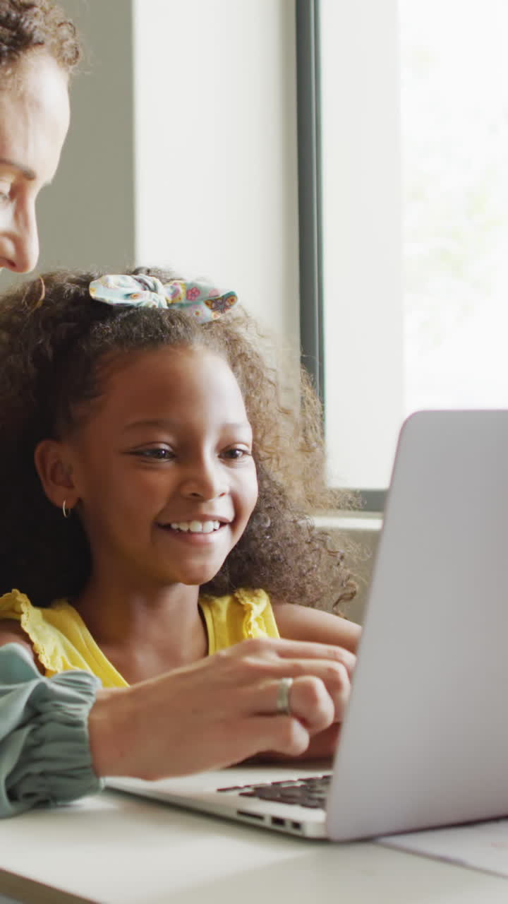 video de una feliz maestra caucásica explicando la lección en una computadora portátil a una chica afroamericana