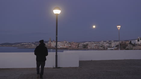 city scape, man enters, takes photos of coastal town, as moon shines above