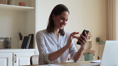 mujer joven con un mensaje de texto de teléfono inteligente sentada en la oficina del hogar