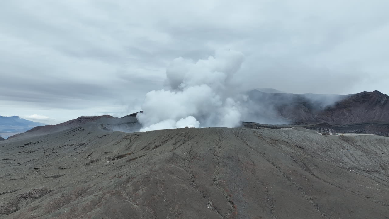 화산에서 연기가 아오르는 일본의 아소 산의 공중 풍경, 화산에 접근하는 영화적인 드론 비행에서 포착되었습니다.