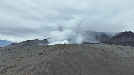 vista aérea del monte aso en japón, con humo que se eleva desde el volcán, capturado en un vuelo cinematográfico de drone que se acerca al volcán