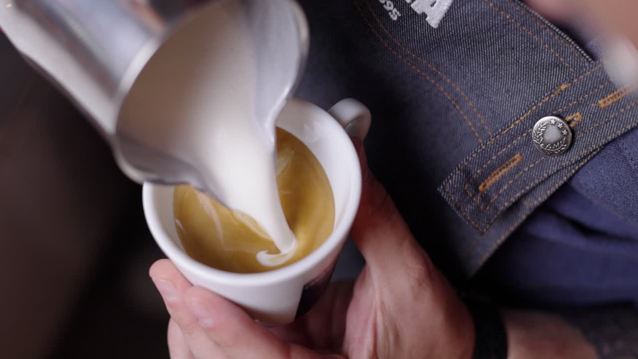 Slowmotion barista making cappuccino leave latte art with freshly Italian brewed espresso in white ceramic cup