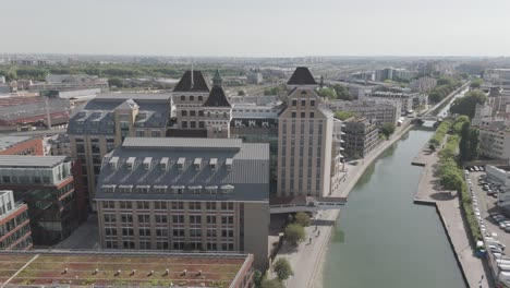 drone shot pulling away from grands moulins de pantin and canal with paris skyline in view - france