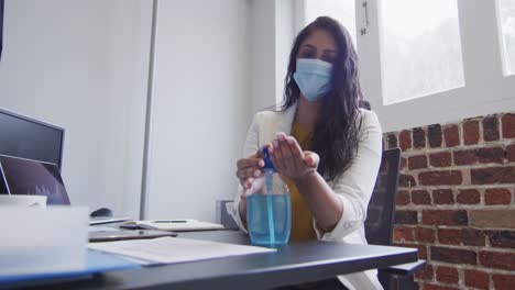 mujer con máscara facial desinfectando sus manos en la oficina