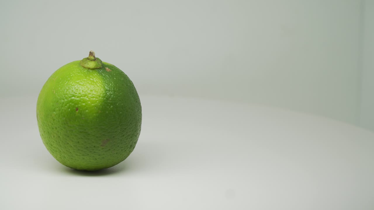limas agrias verdes fruta girando en el sentido de las agujas del reloj en el lado izquierdo del plato giratorio con fondo blanco puro - toma de primer plano