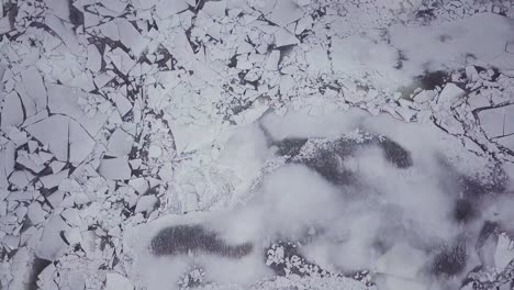 top down drone shot flying above snowy river with big ice chunks during a winter storm in connecticut