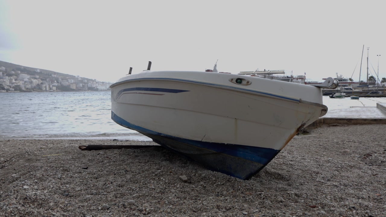 Vista ravvicinata di una piccola barca a motore bianca spiaggiata sulla riva di ciottoli della Baia di Saranda