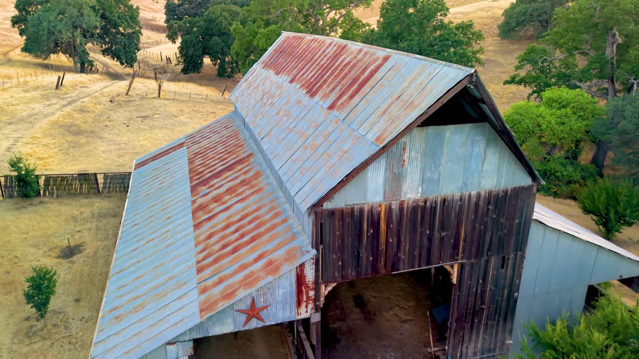A beautiful aerial shot of a rustic, old barn nestled in a valley on a California ranch. The warm light of golden hour illuminates the peaceful, idyllic scene