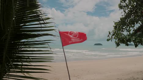 playa tropical con bandera roja que advierte que no se puede nadar, palmeras en primer plano, paisaje escénico