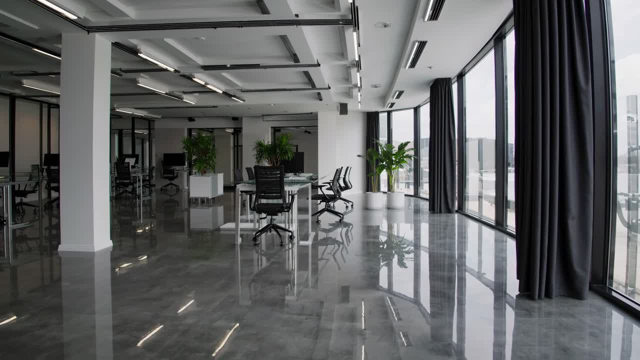 Wide-angle video shot of a modern, open-plan office with sleek design, large windows, and reflective