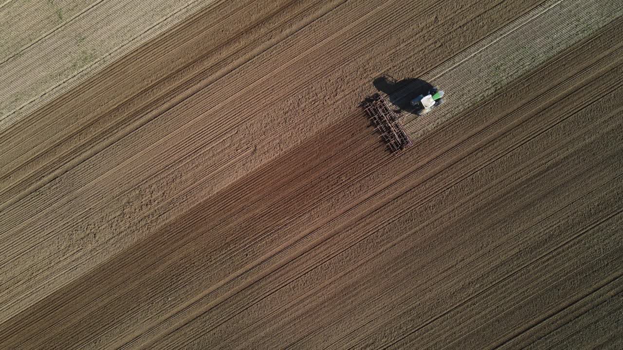Una vista aerea di un trattore che lavora su un grande campo agricolo, arando il terreno in file dritte e parallele.