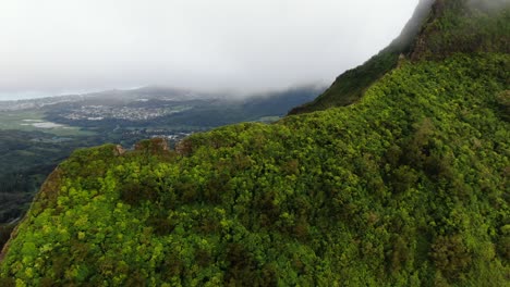 drone flying over hawaiian mountain overlooking east oahu town on a rainy day