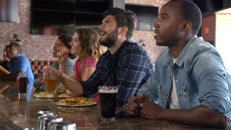 grupo de amigos viendo el juego en la barra de deportes en las pantallas