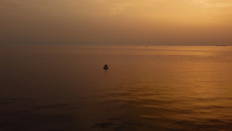 Vista-Aérea-De-Drones-Volando-Hacia-Un-Yate-De-Vacaciones-Barco-De-Pesca-Por-La-Hermosa-Bahía-Naranja-Puesta-De-Sol-Junto-Al-Mar-En-El-Idílico-Mar-Mediterráneo-Adriático-Junto-A-La-Costa-Croata-Con-Islas