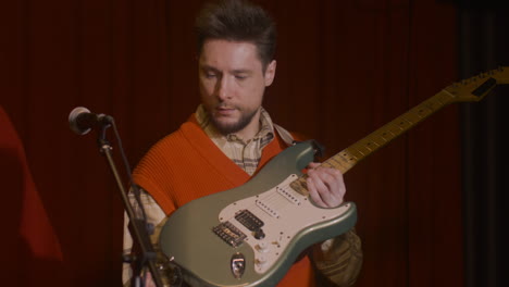 male guitarist plugging jack into electric guitar and tuning before live performance