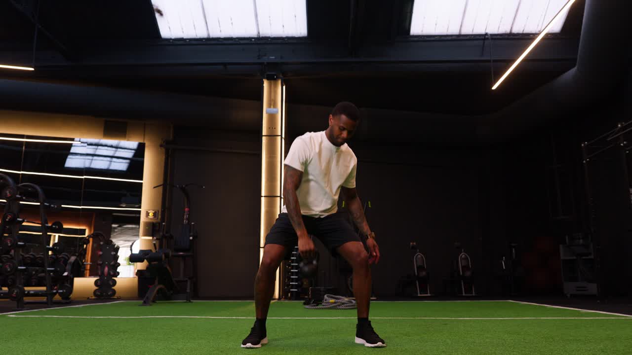 Atletisk mand udfører kettlebell swings i et moderne fitnesscenter