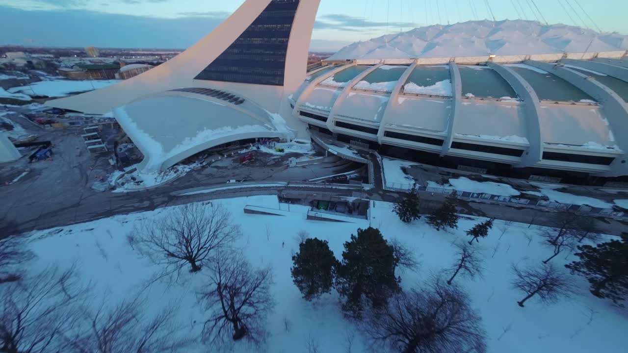 FPV drone circles Montreal’s Olympic Stadium, capturing snowy roof and sunset winter light