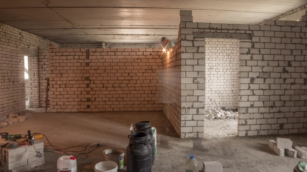 Muratori che posano pareti in mattoni all'interno di un appartamento con attrezzi professionali in timelapse. Operai al lavoro, muratori che costruiscono un muro, appaltatore e operaio. Materiali da costruzione intorno.