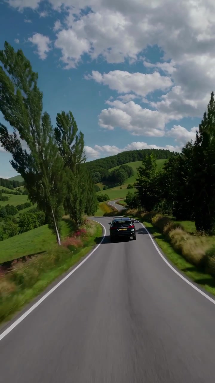 Auto nera che percorre una strada tortuosa attraverso colline verdi