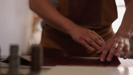 man with apron unrolls brown leather on table in workshop