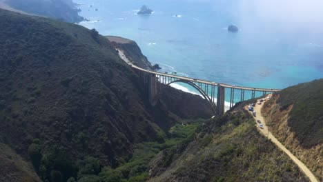 cars traveling bixby canyon bridge on big sur california coast, aerial drone