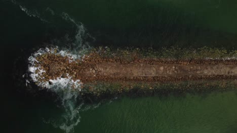 rocky breakwater jetty in ocean, aerial drone top down view