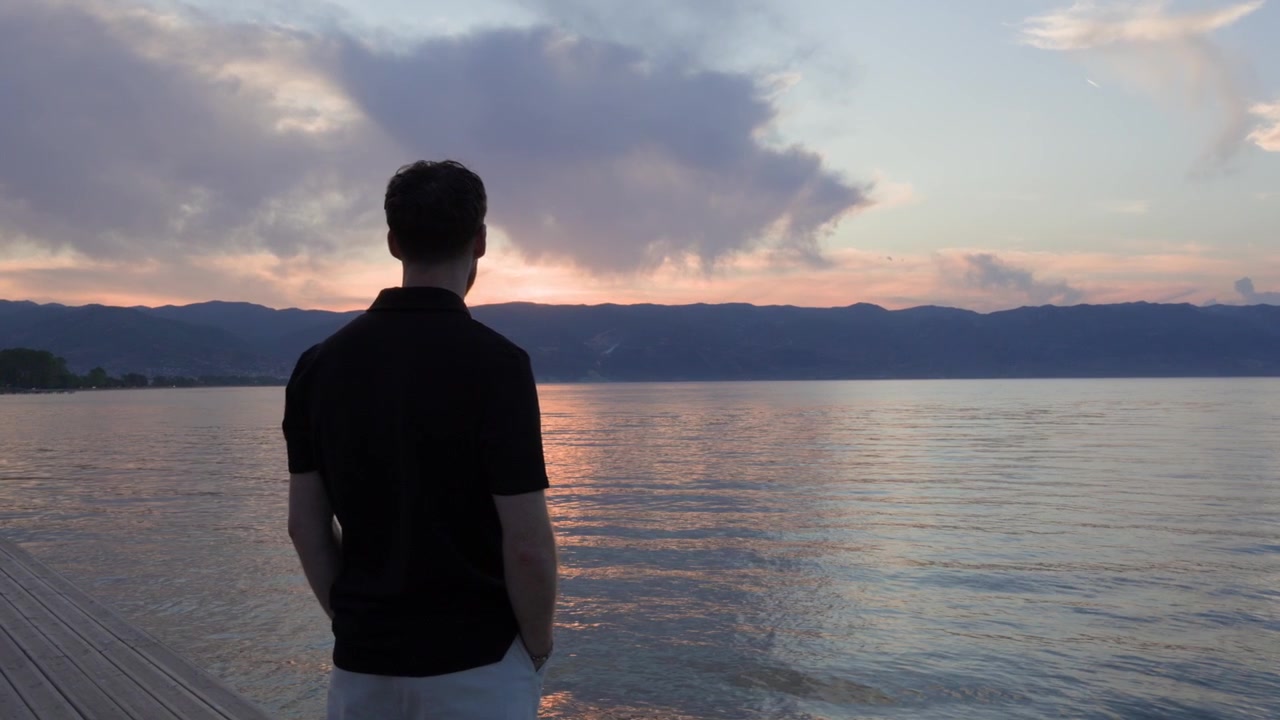Uomo elegantemente vestito in piedi sulla riva del molo che guarda il Lago di Ocrida in Albania