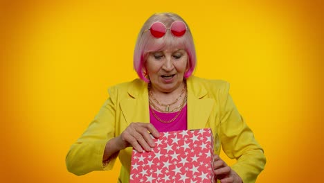 una abuela anciana abriendo una caja de regalos expresando decepción, disgusto gesto a un presente horrible