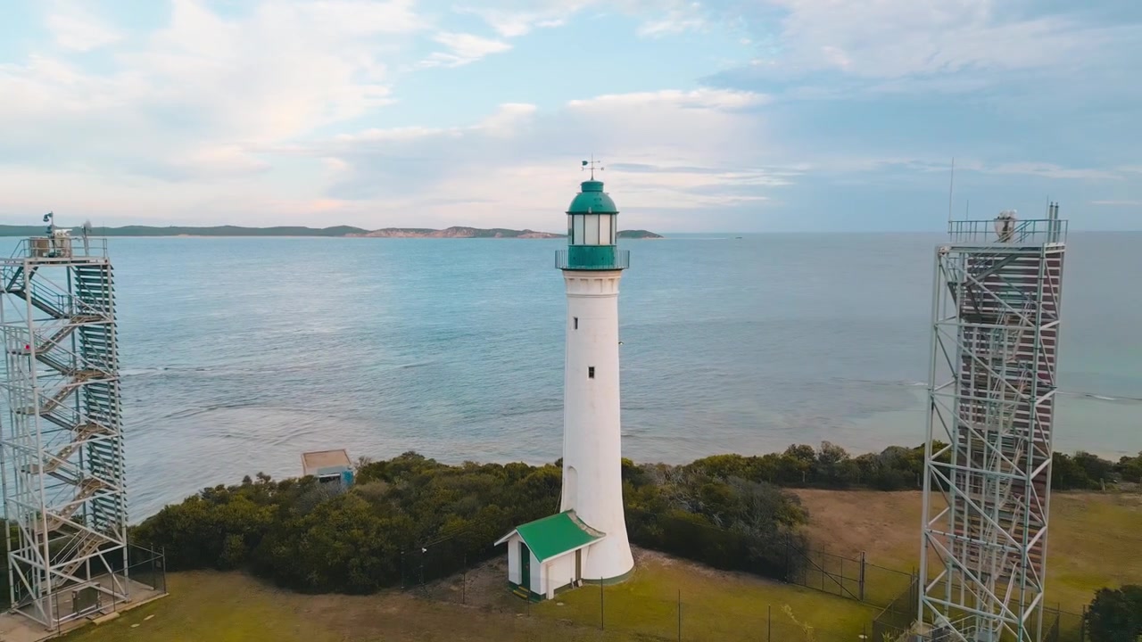 Filmato cinematografico 4K con drone che si muove verso l'alto e si allontana dal faro di Queenscliff, affacciato sullo Stretto di Bass, con la penisola di Mornington visibile all'orizzonte sotto i cieli serali