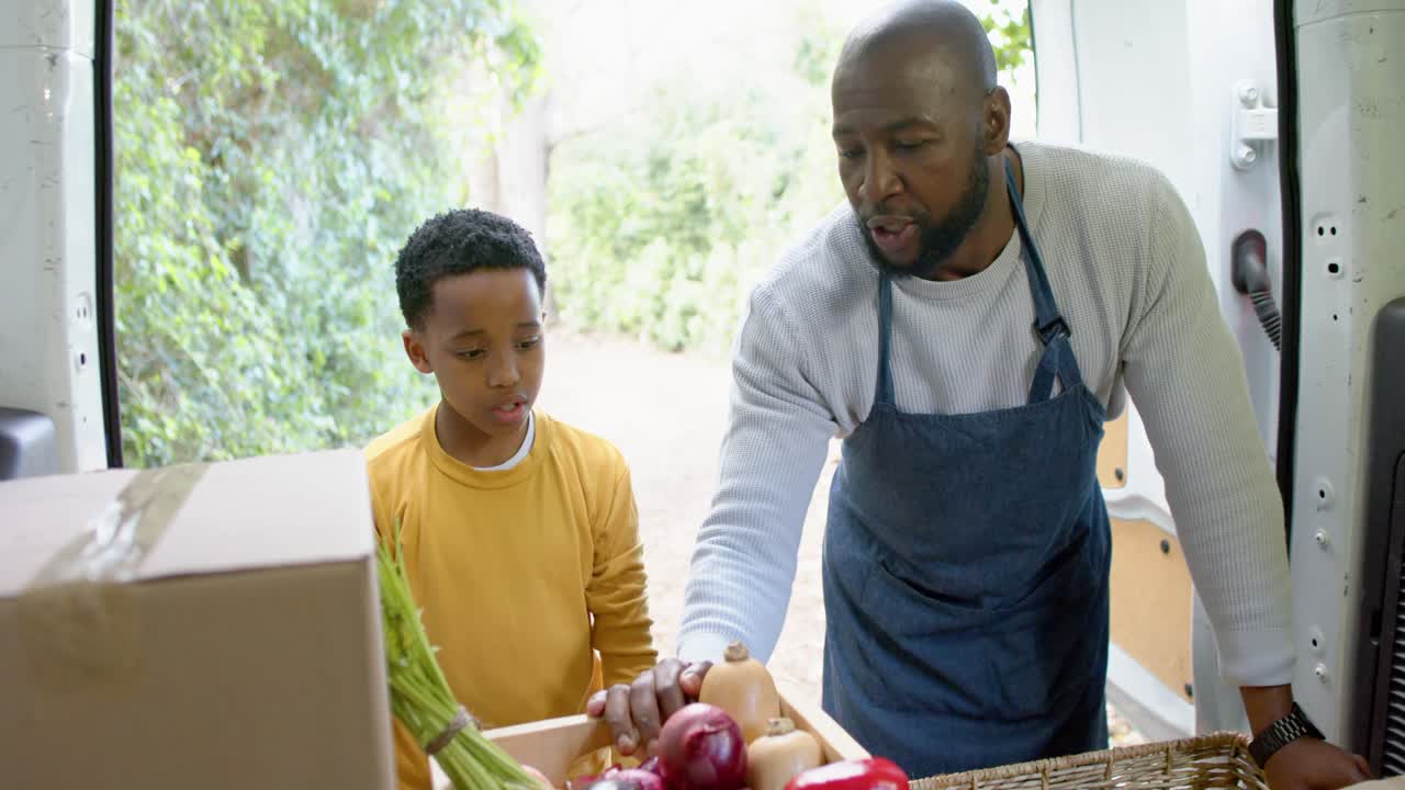 African American father and son standing at van while father picking onion and arranging vegetables