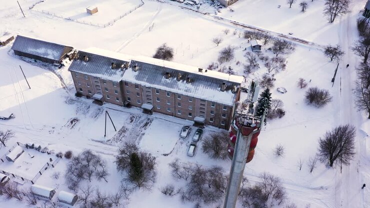 Small apartment building and tall tele communication tower in winter season, aerial ascend shot